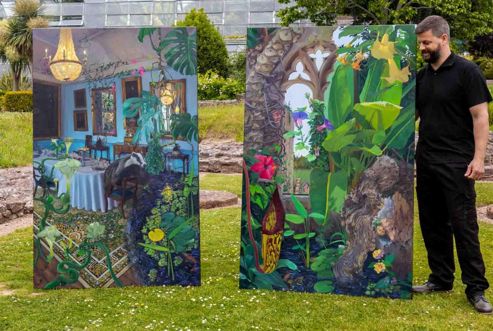 Photograph of artist James standing in the gardens at Torre Abbey with two large oil paintings created during the residency for the void space.
